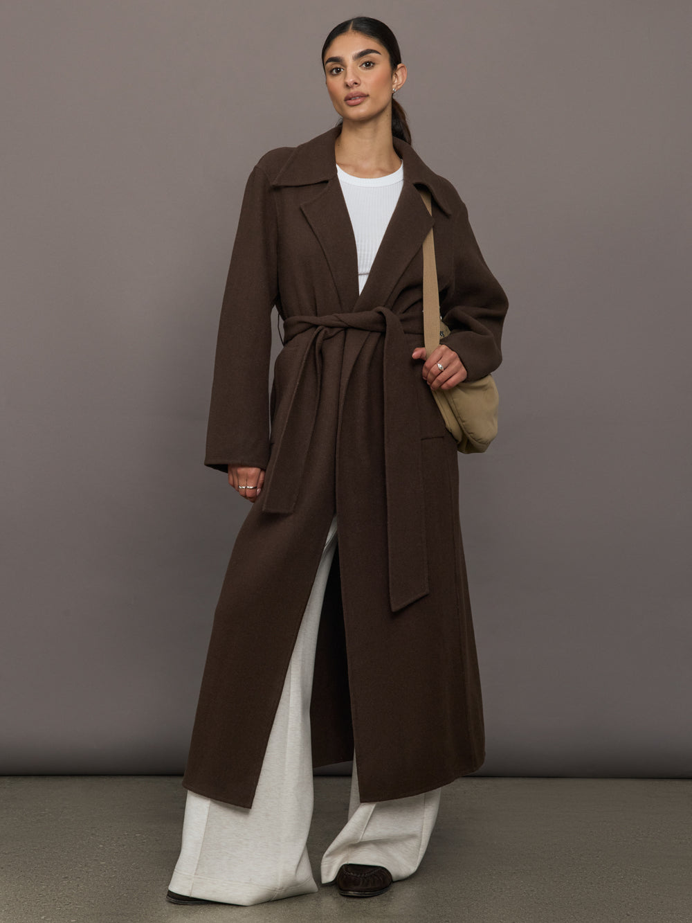 Model is wearing the belted maxi coat in brown with bag, full body.
