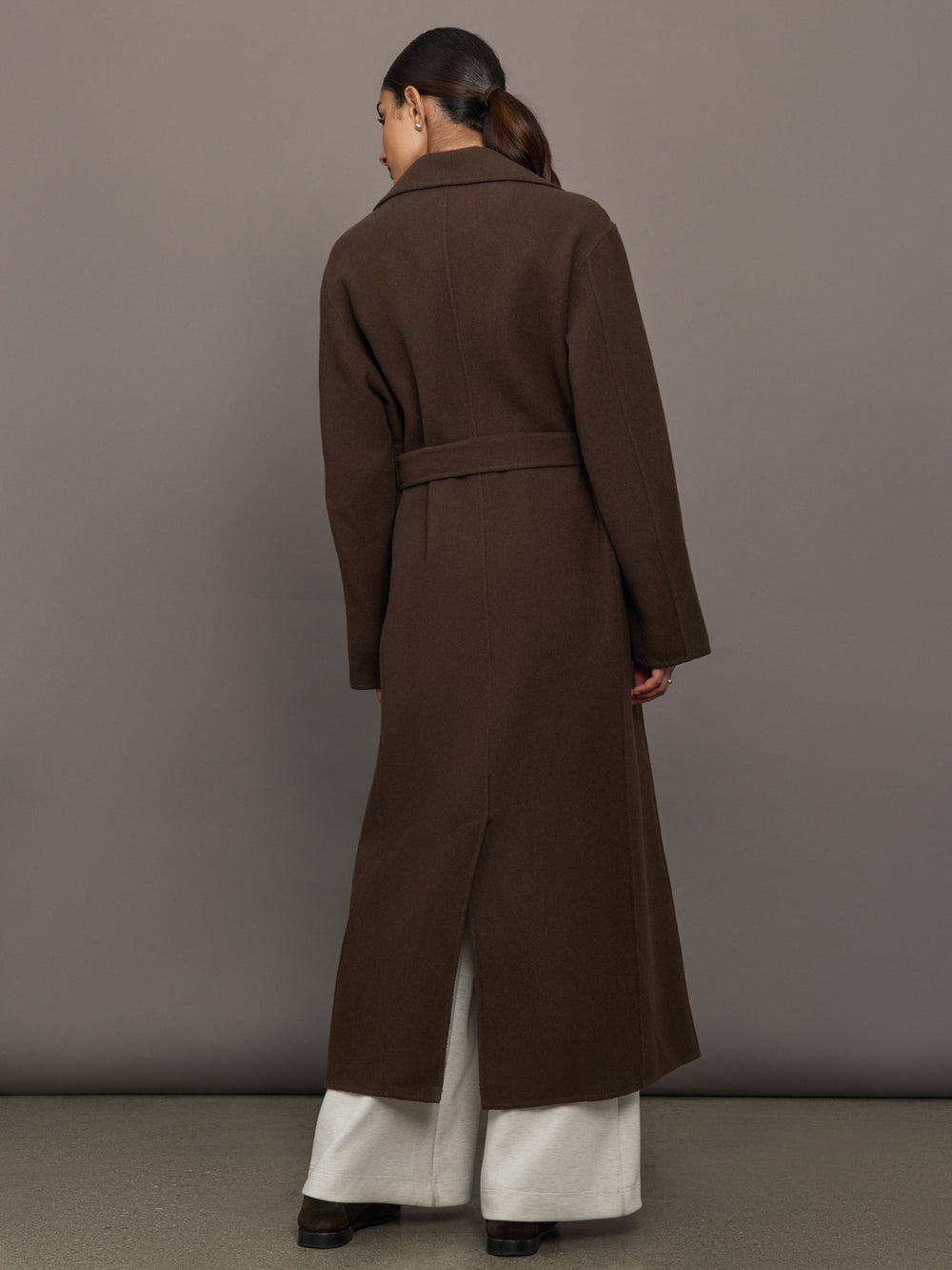 Model is wearing the belted maxi coat in brown, back view.