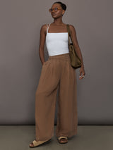 Model is wearing the Coconut cupro pleated wide leg pant styled with white tank, full outfit view.