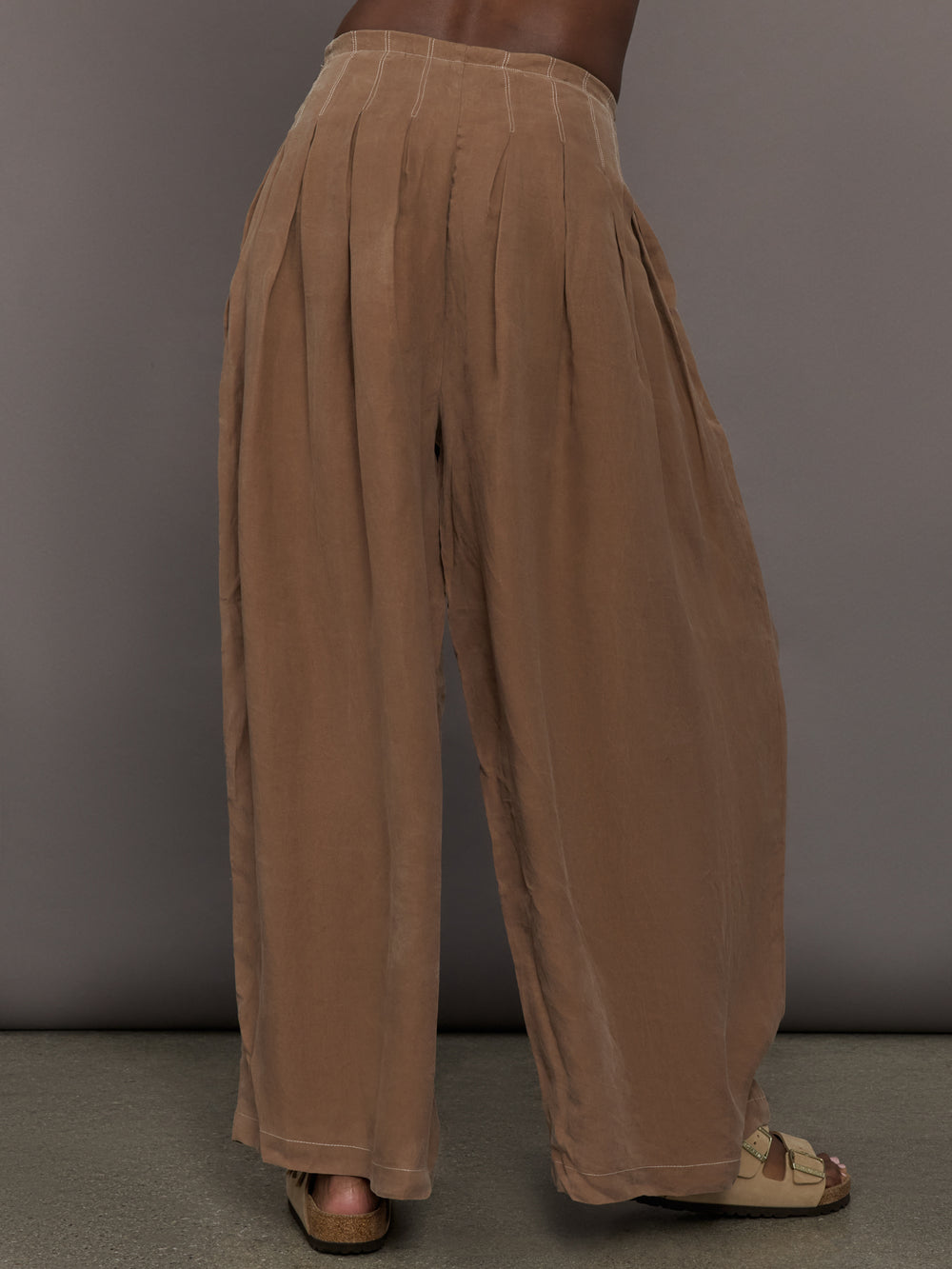 Back view of the Coconut cupro pleated wide leg pant in brown, showing the relaxed drape, wide pleats, and waistband detail.