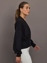 Model is wearing a black ribbed-waist cardigan with blouson sleeves, cinched waistband, and cropped fit, side view.
