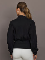 Model is wearing a black ribbed-waist cardigan with blouson sleeves and fitted ribbed waistband, back view.