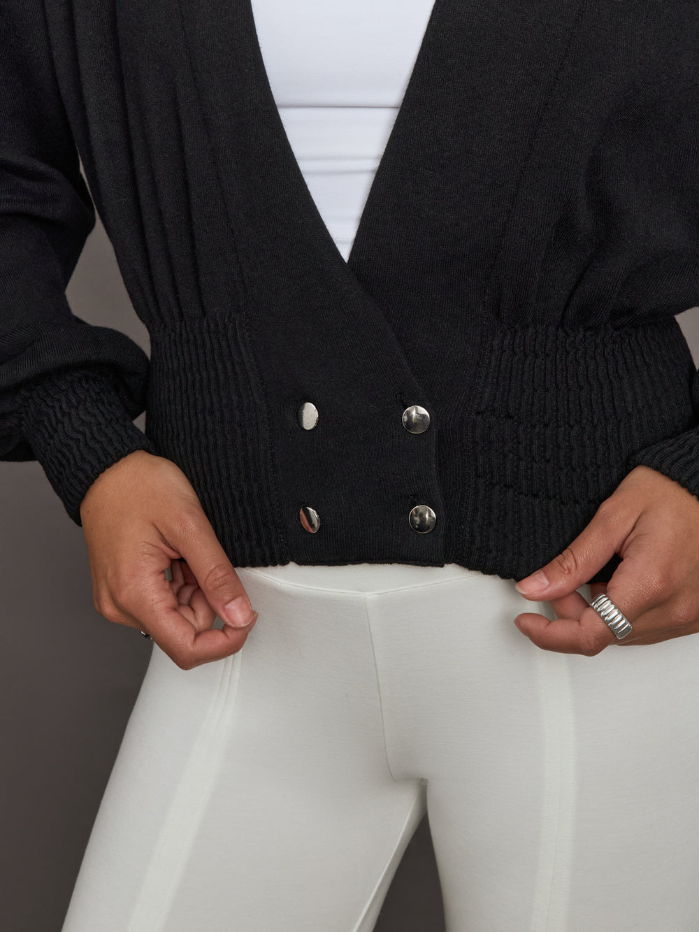 Close-up of black ribbed-waist cardigan showing ribbed waistband and silver button detail, front view.