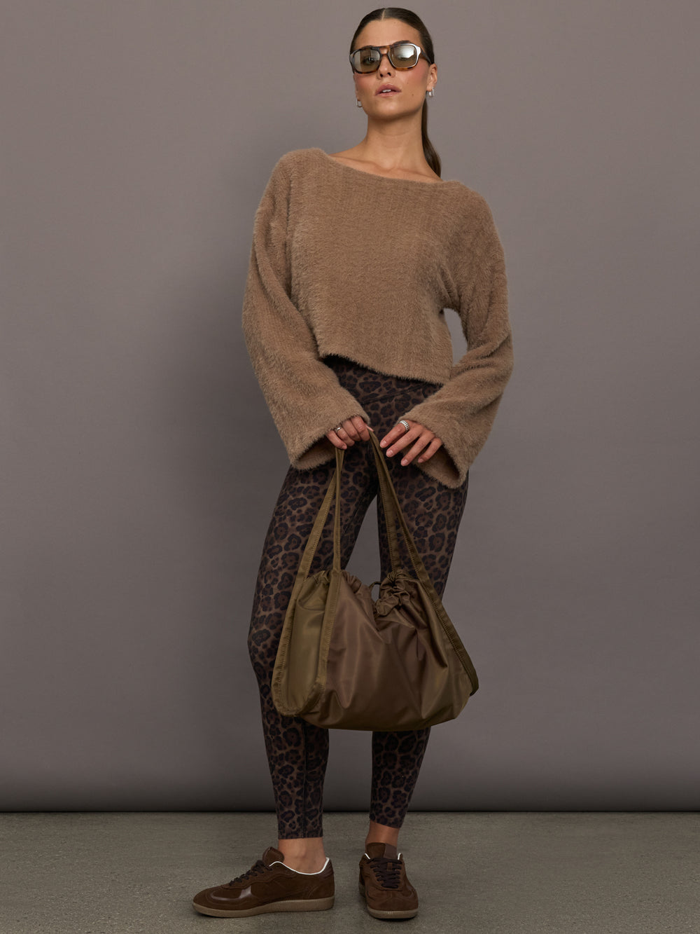 Model is wearing a taupe plush long-sleeve top with wide bell sleeves, styled with leopard print leggings, brown sneakers, oversized sunglasses, and an olive shoulder bag, front full body view.