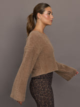 Model is wearing a taupe plush long-sleeve top with wide bell sleeves and relaxed fit, styled with leopard print leggings, side view.