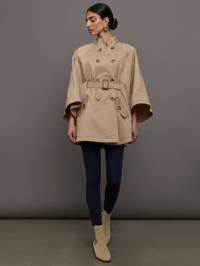 Model wears a tan high neck bell sleeved trench with double breasted buttons and a belted high waist. 