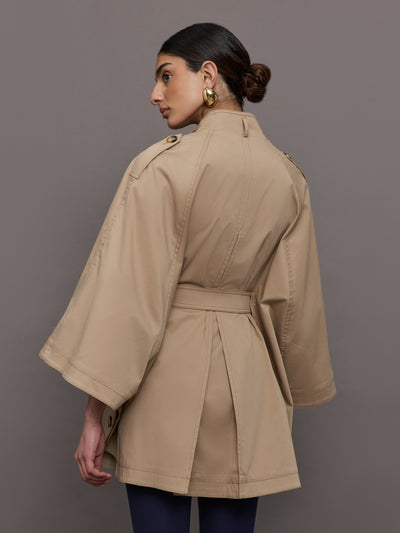 Model wears a tan high neck bell sleeved trench with double breasted buttons and a belted high waist. 