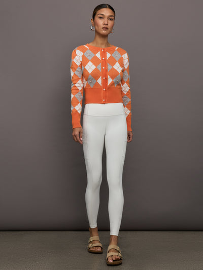 Model wears an orange cardigan with white and gray argyle print and pearls centered over each argyle. 