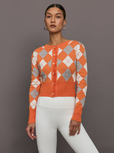 Model wears an orange cardigan with white and gray argyle print and pearls centered over each argyle. 