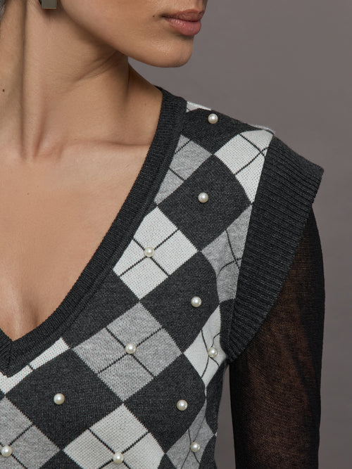 Model wears a gray argyle short sleeved V neck sweater with long black sheer sleeves. 