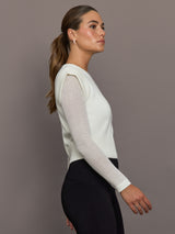 Model is wearing a white crew-neck sweater with sheer mesh sleeves and ribbed hem, showing slim fitted profile, side view.