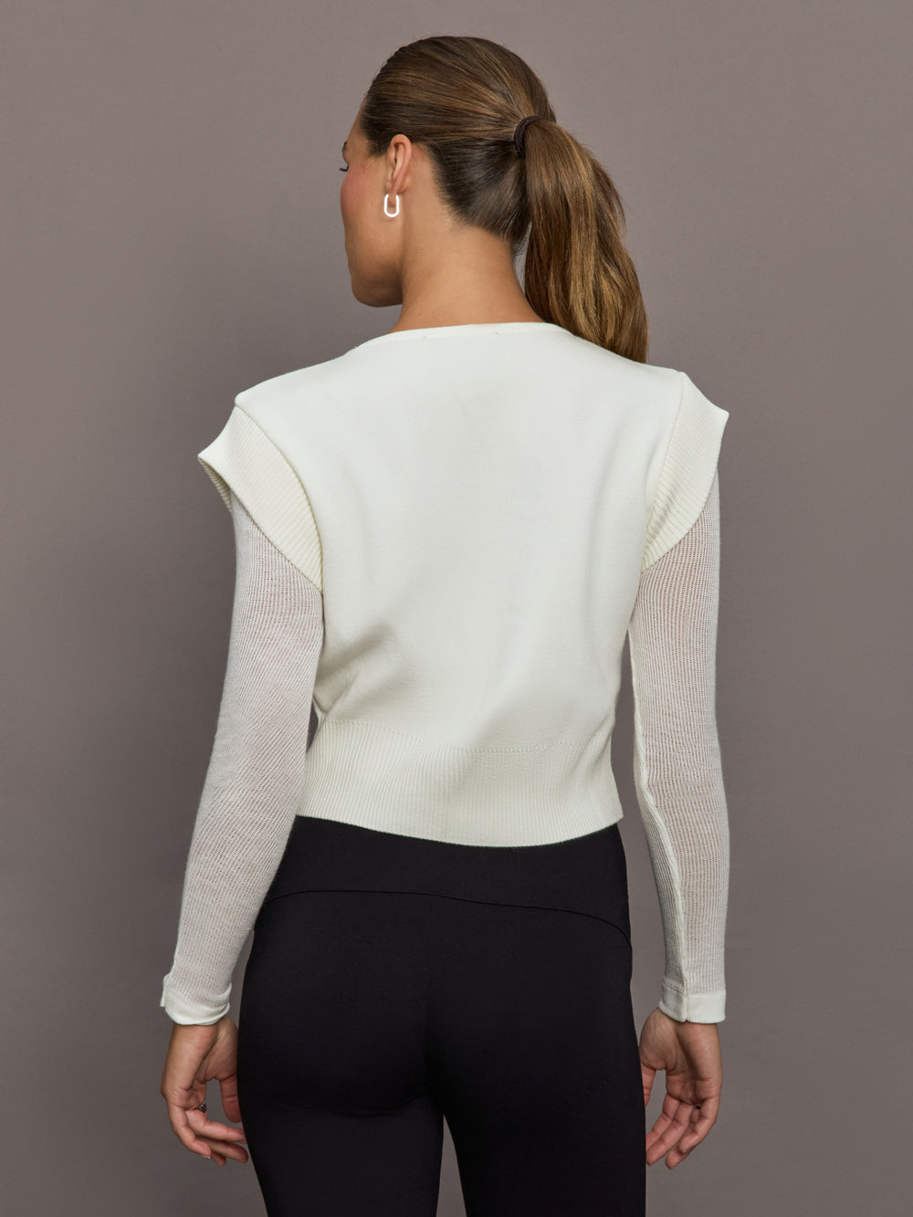 Model is wearing a white crew-neck sweater with sheer mesh long sleeves and straight back hem, back view.