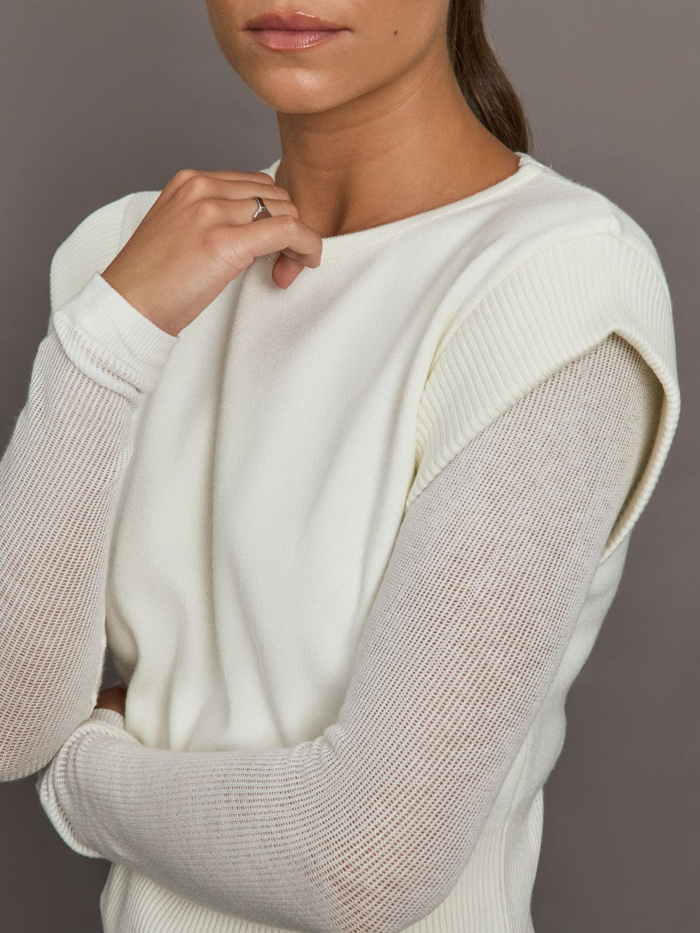 Close-up of white crew-neck sweater highlighting sheer mesh knit sleeves and ribbed shoulder detail, front view.