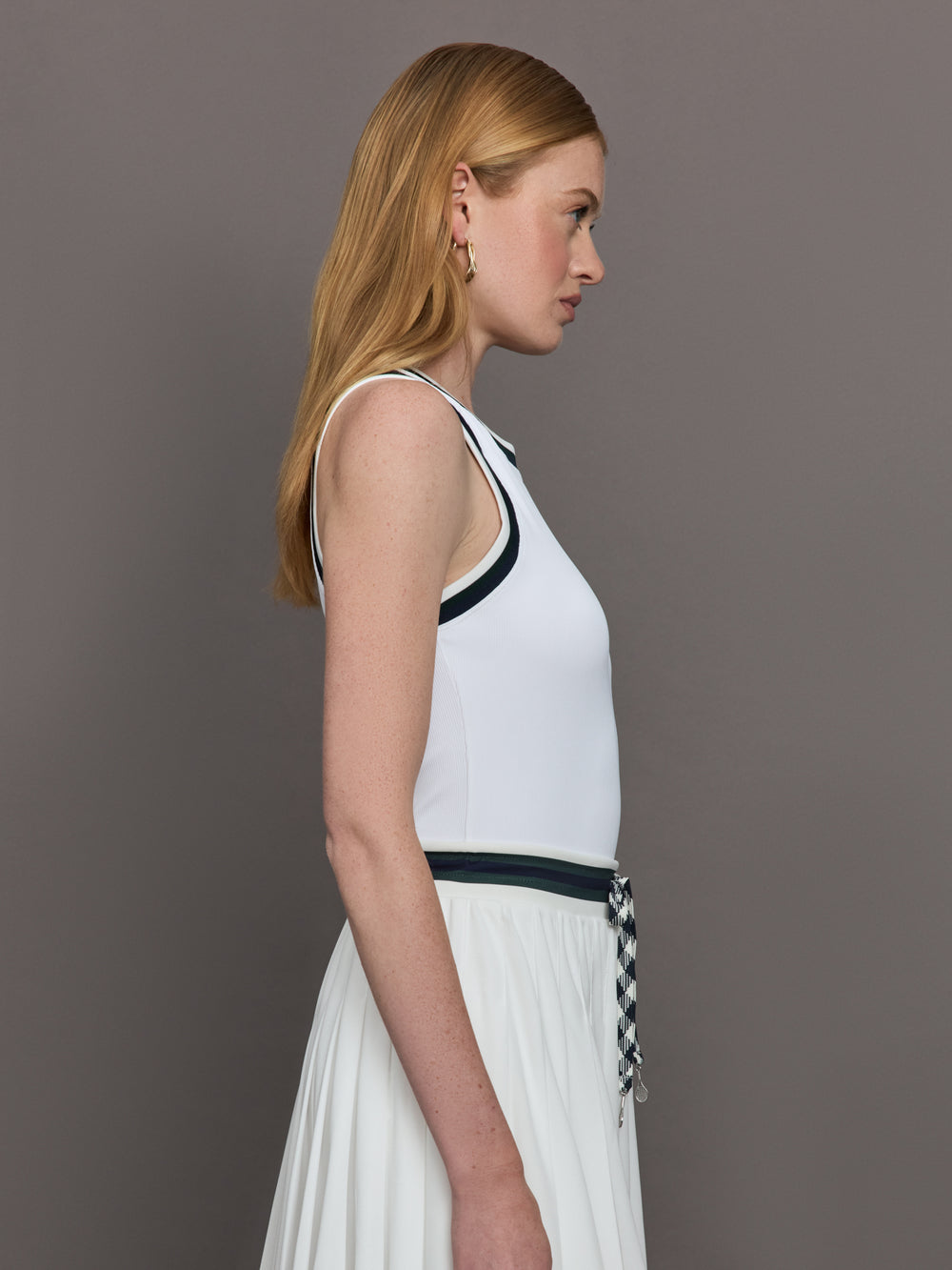 Model wears a white tank top with green trim, perfect for tennis. 