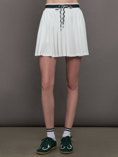 Model wears a pleated white tennis skirt with green drawstrings. 