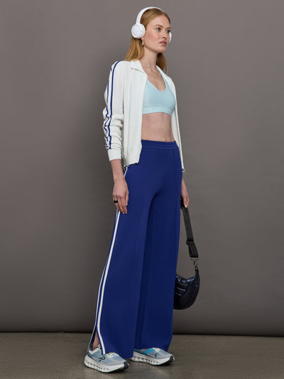 Model wears a white track jacket with blue racing stripes down the sides of arms.