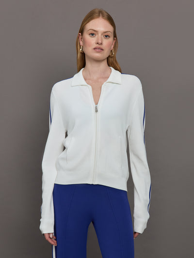 Model wears a white track jacket with blue racing stripes down the sides of arms.