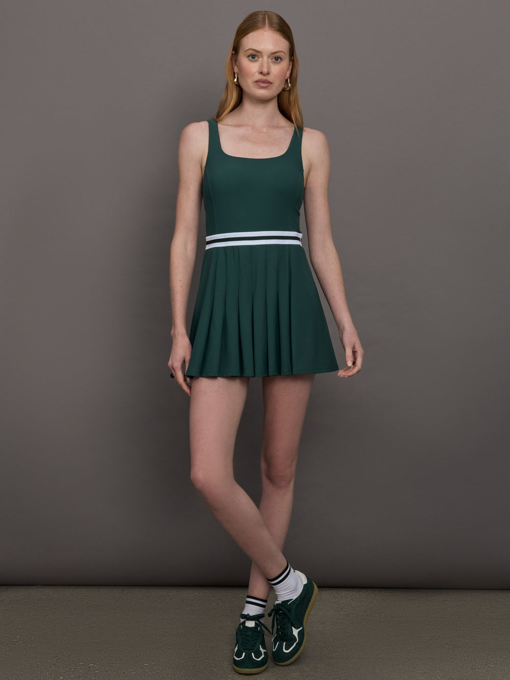 Model wears a dark green wide scoop neck tennis dress with pleating and a white waistline.