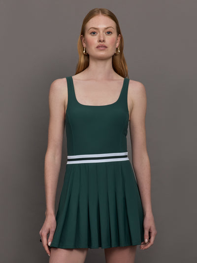 Model wears a dark green wide scoop neck tennis dress with pleating and a white waistline.