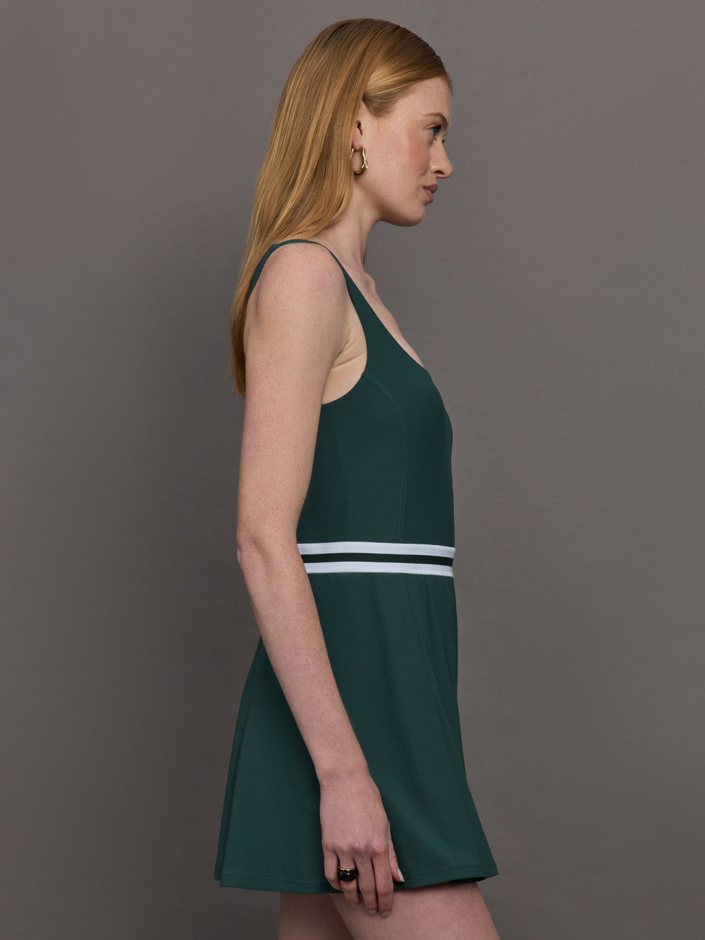 Model wears a dark green wide scoop neck tennis dress with pleating and a white waistline.