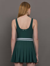 Model wears a dark green wide scoop neck tennis dress with pleating and a white waistline.