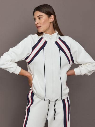 Model wears The Pacific Morgan Zip Up Jacket in white with a sleek, sporty design with a full front zipper, high collar, and navy and red detailing.