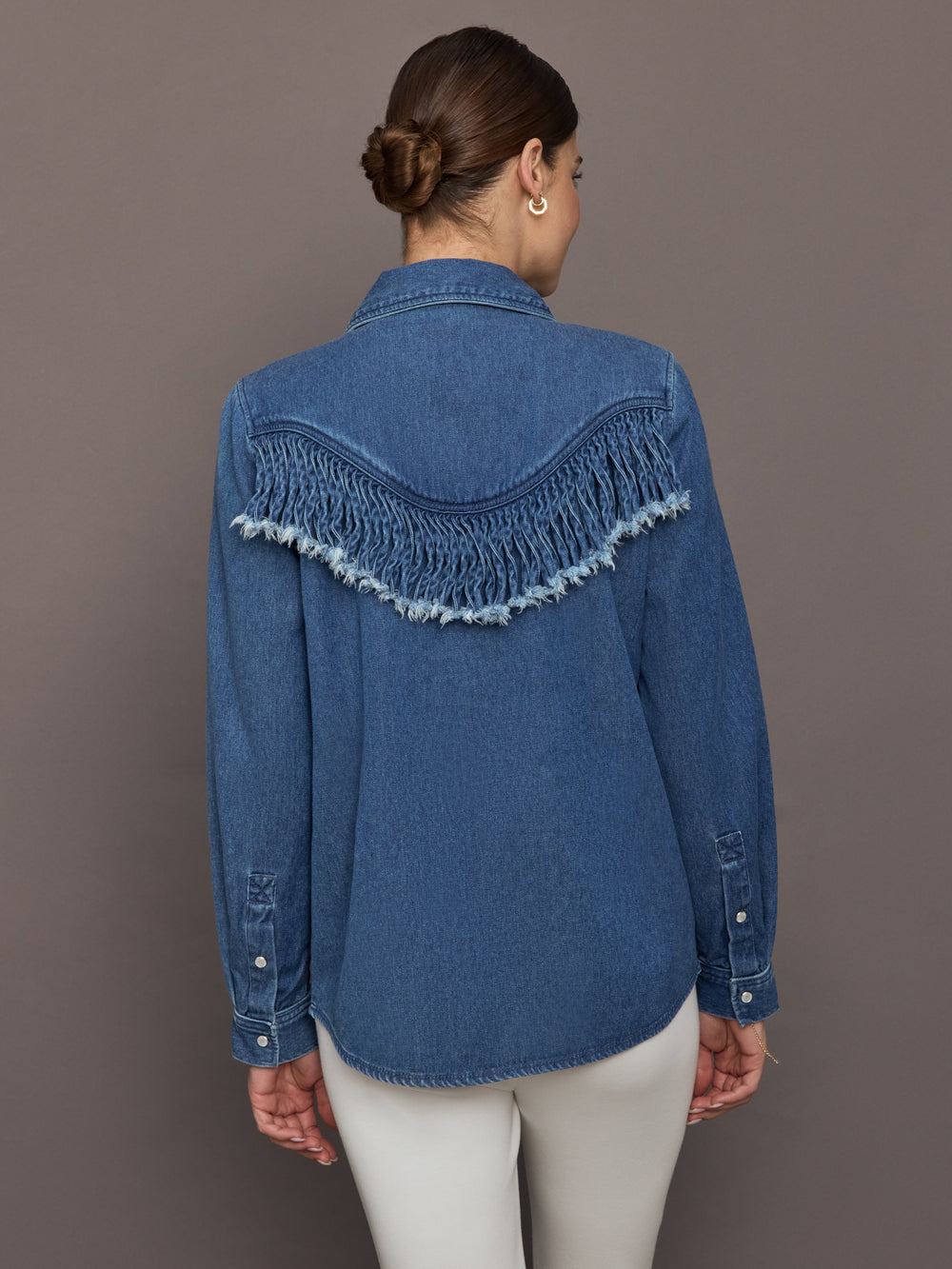 Model wears the Wildwest Style Fringe Shirt in blue denim with classic western-inspired fringe detailing across the chest and back and a button-up front.