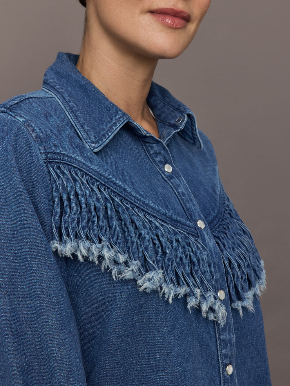 Model wears the Wildwest Style Fringe Shirt in blue denim with classic western-inspired fringe detailing across the chest and back and a button-up front.
