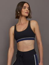 Model wears black racerback sports bra with a scoop neckline and brown, white and navy detailing.