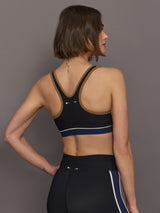 Model wears black racerback sports bra with a scoop neckline and brown, white and navy detailing.