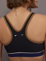 Model wears black racerback sports bra with a scoop neckline and brown, white and navy detailing.