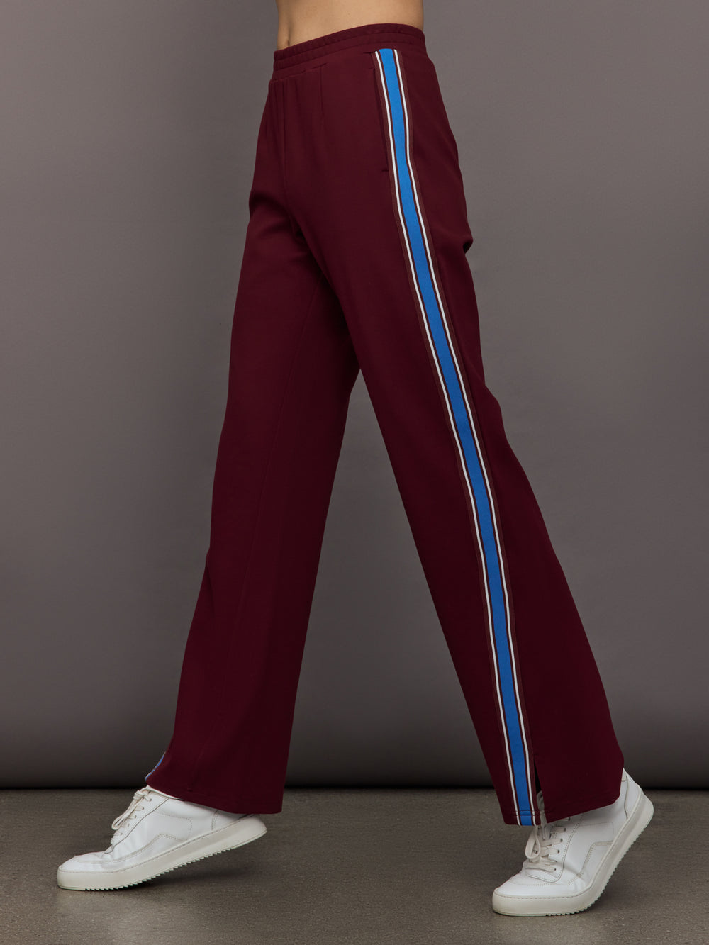 Model wears maroon pants with a blue stripe on each side.