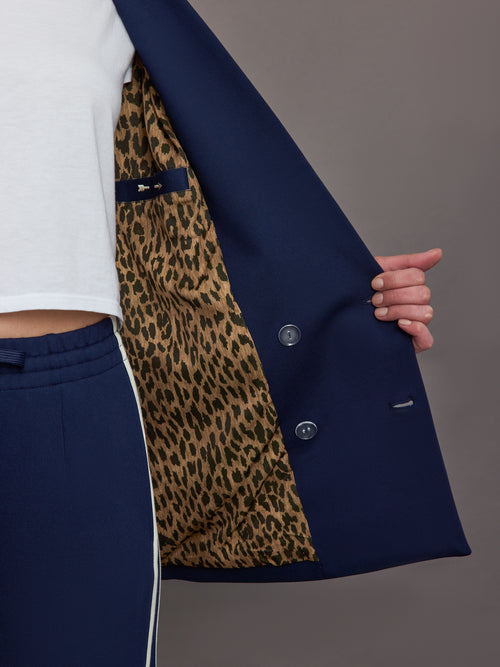 Model wears classic navy double-breasted blazer featuring structured shoulders and leopard detailing inside.
