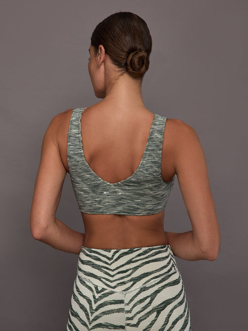 Person wearing a green sports bra and zebra print leggings against a gray background