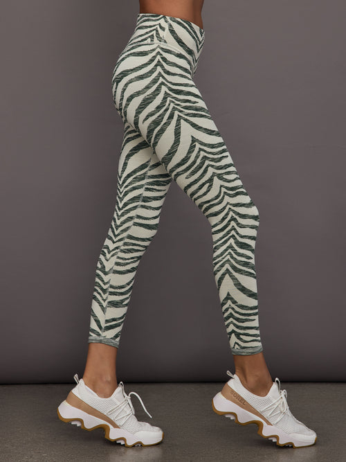Person wearing zebra print leggings and white sneakers on a dark background