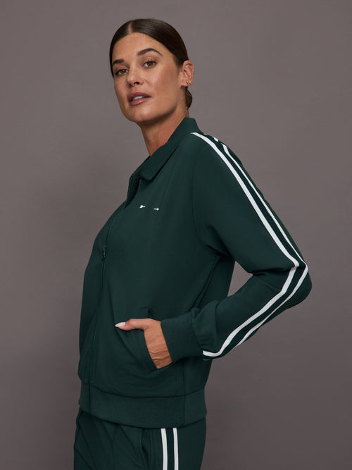 Woman wearing a green tracksuit with white stripes on a gray background