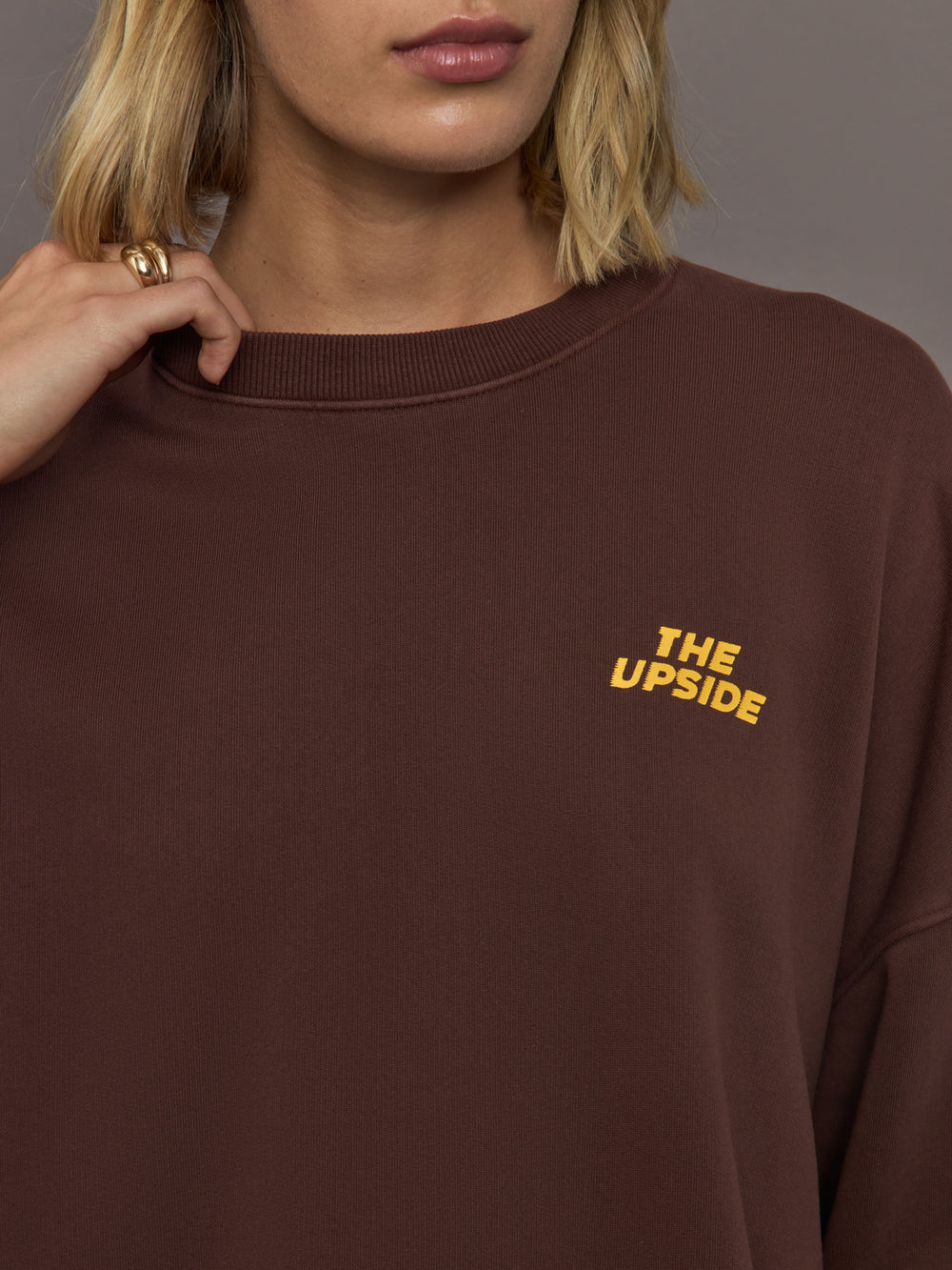 Model wearing a brown sweatshirt with 'The Upside' logo