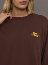 Model wearing a brown sweatshirt with 'The Upside' logo