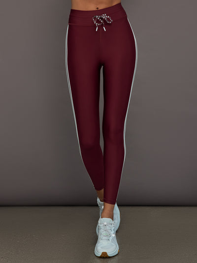 Model wears a pair of high rise burgundy leggings with contrast stripe down side. 