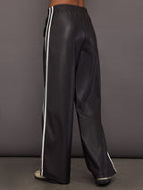 Model wears a pair of dark brown vegan leather track pants with white stipes down side. 