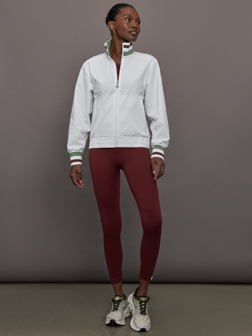 Model wears white track jacket with a high collar, front zipper, and ribbed cuffs and hem.

