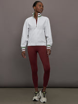 Model wears white track jacket with a high collar, front zipper, and ribbed cuffs and hem.
