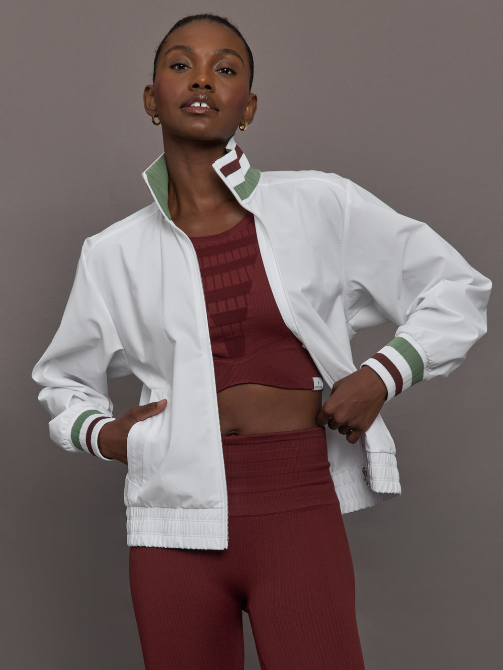 Model wears white track jacket with a high collar, front zipper, and ribbed cuffs and hem.




