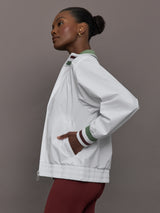 Model wears white track jacket with a high collar, front zipper, and ribbed cuffs and hem.
