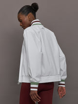 Model wears white track jacket with a high collar, front zipper, and ribbed cuffs and hem.
