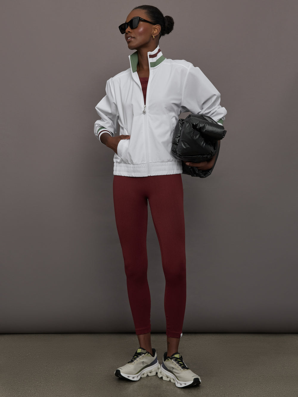 Model wears white track jacket with a high collar, front zipper, and ribbed cuffs and hem.
