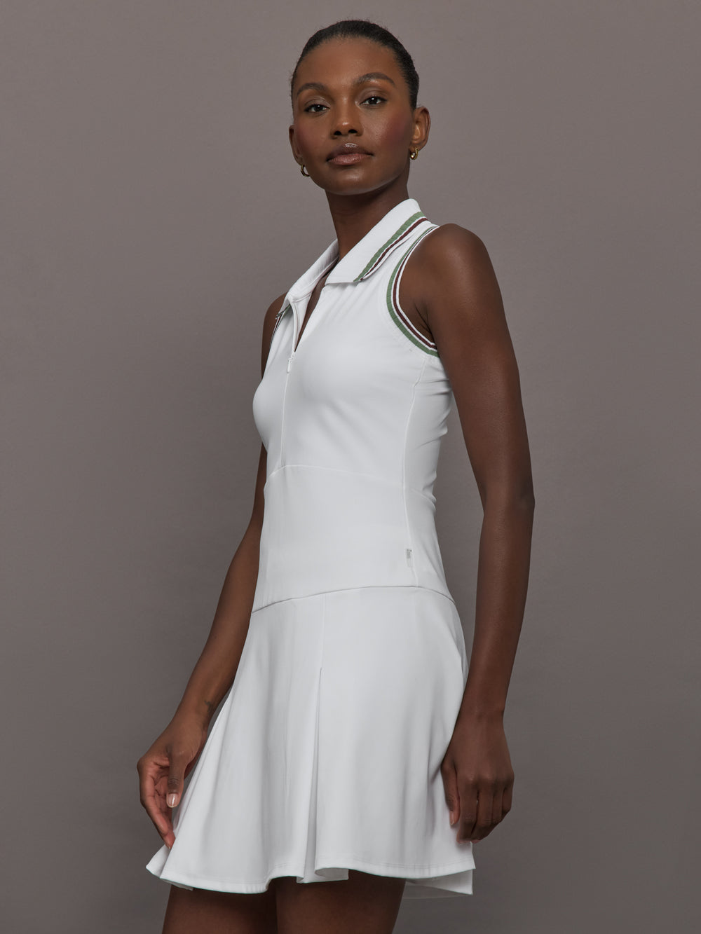 Model wears white sleeveless dress with a fitted bodice and flared skirt, and a collared neck.
