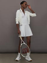 Model wears white sleeveless dress with a fitted bodice and flared skirt, and a collared neck.
