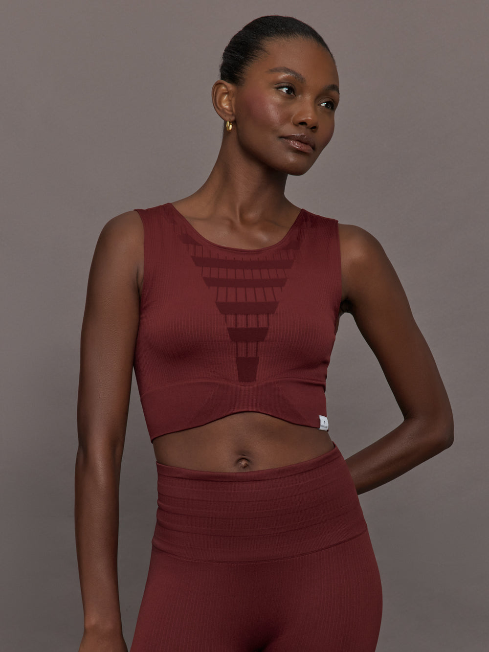 Model wears sports bra in Terracotta with a high neckline and a subtle patterned detailing in the center front.




