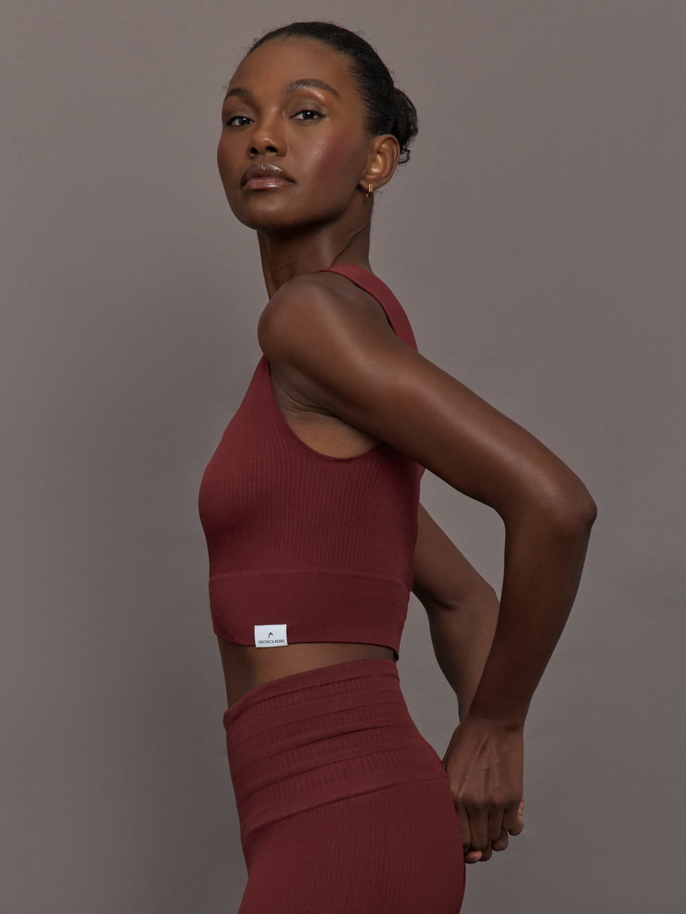 Model wears sports bra in Terracotta with a high neckline and a subtle patterned detailing in the center front.
